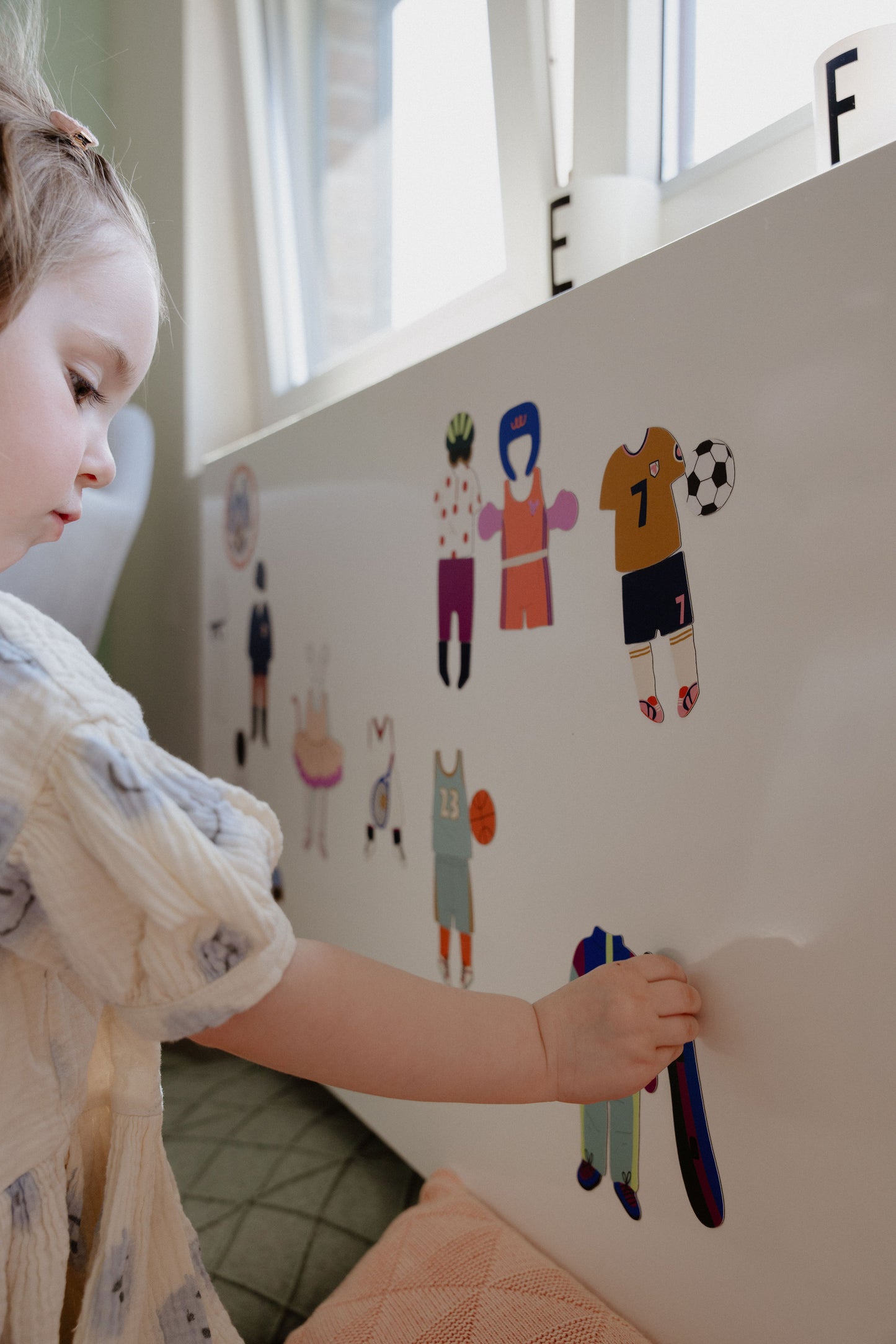 Petite fille jouant au jeu magnétique Les Sports sur un tableau blanc, dès 3 ans